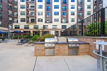A patio with barbecue grills and a building in the background